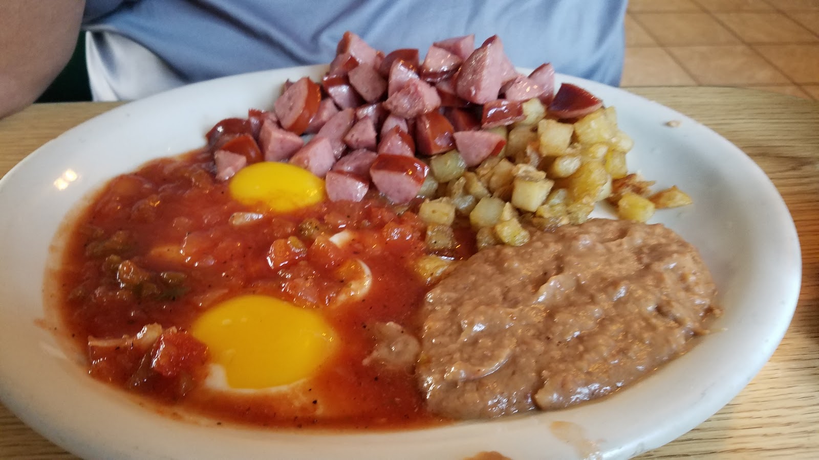 Huevos rancheros plate with eggs, sausage, potatoes, and refried beans
